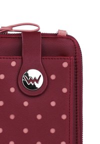 Red leather wallet with pink polka dots, featuring a silver logo button and a matching zipper pull, showcasing smooth texture and rounded shape.