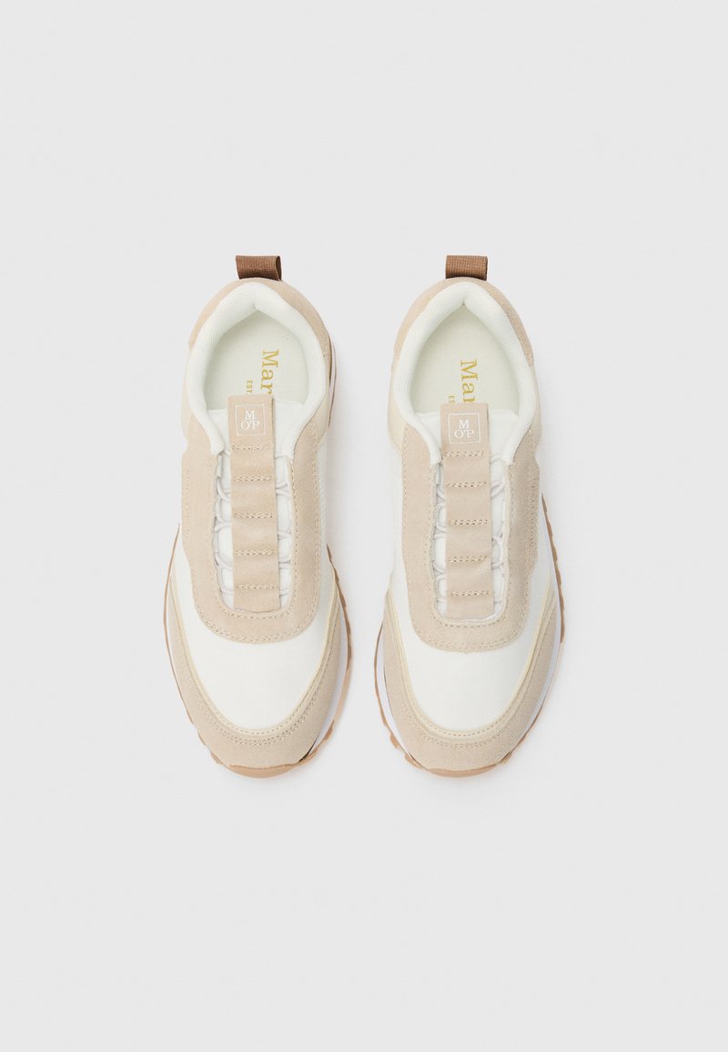 Para beżowo-białych sneakersów wsuwanych z zamszowymi akcentami i pętelkami, widzianych z góry na białym tle.