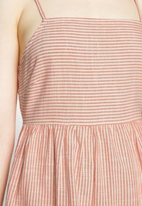 Sukienka na ramiączkach z naprzemiennymi paskami w jasnym brzoskwiniowym i kremowym kolorze, z marszczonym pasem i miękką, lekką teksturą materiału.