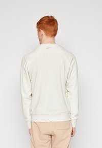 Ljusgrå sweatshirt med långa ärmar och rund halsringning, med en liten logotyp på baksidan. Mjuk textur, avslappnad passform.