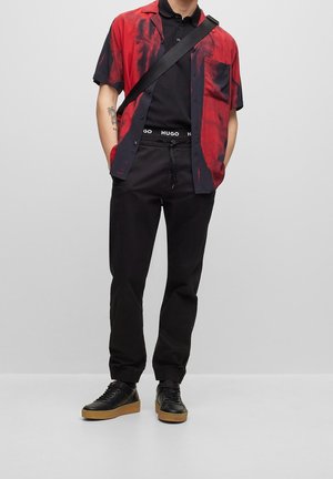 Chemise à manches courtes rouge et noire à motifs, polo noir, pantalon noir avec des poignets élastiques et baskets noires avec des semelles en gomme.