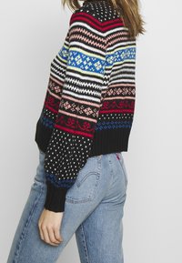 Svart stickad tröja med flerfärgade horisontella ränder och geometriska mönster. Har en ribbad nederkant och ärmar, med en åtsittande silhuett.