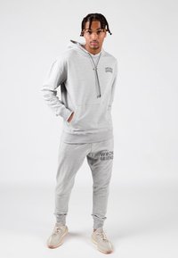 Szary zestaw bluzy z kapturem i spodni dresowych z napisem "WRONG FRIENDS". Bluza ma sznurek ściągający oraz kieszeń kangurkę; spodnie mają ściągacze przy kostkach.