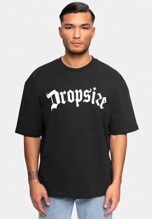 Black oversized T-shirt in cotton, featuring large white Gothic-style text "Dropsie" on the front. Crew neck, short sleeves, relaxed fit.