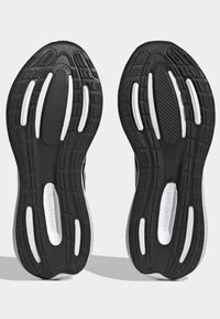 Suelas de zapatillas de running en blanco y negro con amortiguación "Cloudfoam", que cuentan con patrones de agarre texturizados y relieve en la banda de rodadura para tracción.