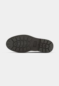 Suela de zapato de goma negra con un patrón texturizado y robusto para un mejor agarre. Presenta un diseño plano con líneas de taco pronunciadas y una marca.