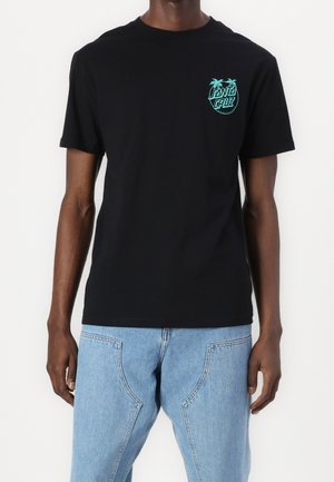 Black T-shirt with small turquoise "Santa Cruz" logo and palm trees on left chest, worn with light blue denim jeans.