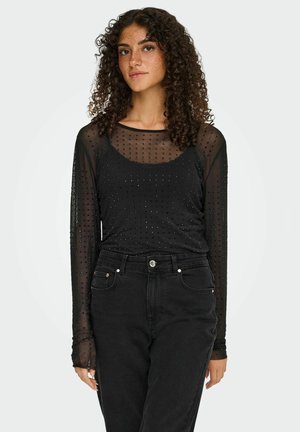 Haut noir à manches longues en tissu en maille à pois, avec un col rond et une coupe ajustée, associé à un jean noir taille haute.