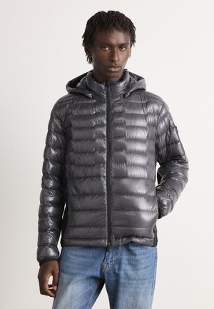 Puffer jacket in shiny, dark gray material, featuring a zippered front, a hood, and horizontal quilted sections. Worn with blue jeans.