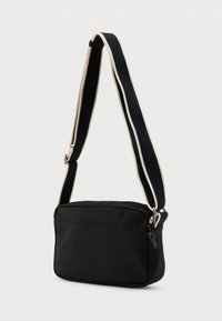 Μαύρη τσάντα ώμου από ύφασμα με ορθογώνιο σχήμα, ρυθμιζόμενο ιμάντα με κρεμ ρίγες και επάνω φερμουάρ κλεισίματος.