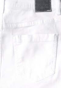 Valkoinen denimpaita, jossa on takatasku suorakulmaisen muotoisena ja näkyvillä saumoilla. Tumma etiketti on kiinnitetty vyötärölle.