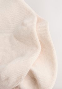 Soft, cream-colored knitted fabric with fine ribbed texture and gentle folds on a light background.
