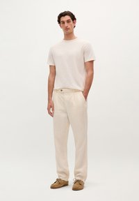 T-shirt di cotone beige chiaro, abbinata a pantaloni in lino crema a vestibilità ampia con una piega frontale e un bottone marrone in vita. Scarpe marroni.