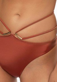 Bikini dolny w kolorze rdzy z wieloma cienkimi paskami i złotymi akcentami. Gładka tekstura i minimalistyczny design, oferujący niską talię.