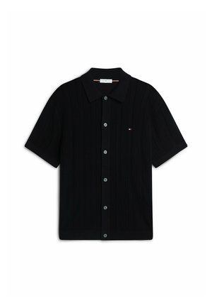 Polo en maille noire à manches courtes avec patte de boutonnage devant et petit logo rouge, blanc et bleu sur le panneau gauche de la poitrine.