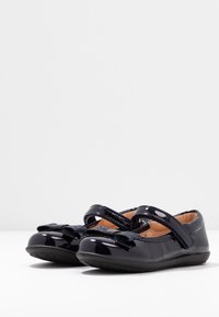 Czarne lakierowane buty typu Mary Jane z błyszczącymi akcentami, zaokrąglonymi noskami i regulowanymi paskami. Gładka faktura z gumowymi podeszwami.