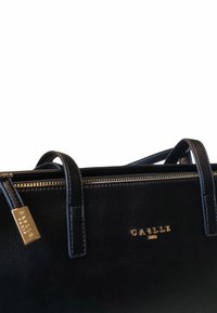 Borsa a mano in pelle nera con chiusura a zip, design strutturato, manici doppi e dettagli in logo e hardware color oro. Texture liscia.