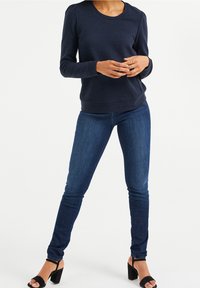 Marineblå texturerad långärmad topp med rund halsringning, matchad med slim fit mörkblå jeans och svarta klacksandaler.