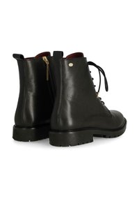 Botas de tobillo de cuero negro con una textura suave, punta redondeada, parte delantera con cordones y un cierre de cremallera lateral. Con una suela robusta negra y detalles en forro rojo.