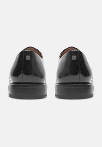 Chaussures en cuir verni noir avec une surface lisse, bout arrondi et un léger talon. Présentent un accent de logo subtil sur le talon.