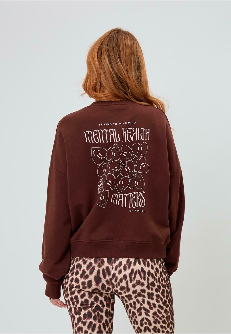 Felpa marrone con stampa grafica che presenta cuori sorridenti e il testo "LA SALUTE MENTALE È IMPORTANTE." Vestibilità slim con maniche a polsino. Leggings con stampa leopardata.