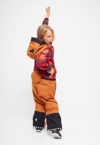 Röd och svart rutig jacka med en orange huva, som är ihop med orangea och svarta snöbyxor med siddragkedjor och rund fickdetalj.