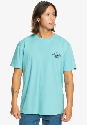 Lyseblåt kortærmet t-shirt lavet af bomuld med rund halsudskæring, der har et marineblåt logo-print på brystet og et mærke på sømmen.