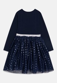 Navy pitkähihaisen mekon, jossa on hopeinen kimalteella varustettu vyötärö ja tulleröijy, jossa on metallisia sydänkuvioita. Pehmeä kangas, jossa on rypistetty pinta.