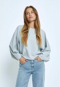 Heller grauer Langarm-Sweatshirt mit strukturiertem Finish, lockerer Passform und überschnittenen Schultern, kombiniert mit hochgeschnittenen blauen Jeans.