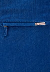 Μπλε ύφασμα από τζιν με διακριτική υφή. Διαθέτει μια μικρή, ραμμένη ετικέτα με το λογότυπο Calvin Klein στην κάτω δεξιά γωνία.