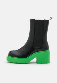 Czarne skórzane botki na kostkę z elastycznymi panelami bocznymi, z wyrazistą zieloną platformą i obcasem. Gładka tekstura, zaokrąglony design noska.