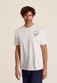 Witte katoenen t-shirt met een ronde halslijn en korte mouwen, voorzien van een kleurrijke zeilbootafbeelding op het linkerborstgedeelte.