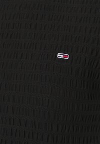 Black textured fabric with a small stitched rectangular logo featuring white, red, and navy blue horizontal stripes.