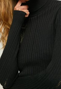 Svart ribbad polotröja med långa ärmar, texturerat tyg och en åtsittande design som framhäver vertikal ribbning och tumhål.