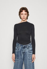 Cămașă lungă neagră cu decolteu tip barcă și detalii pliate, purtată cu blugi ușori de denim, cu talie înaltă și croială largă.