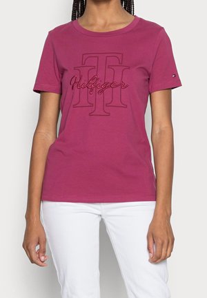 Magentafarbenes Baumwoll-T-Shirt mit Rundhalsausschnitt, kurzen Ärmeln und einem geprägten Logo in der Mitte mit kontrastierenden Nähten.