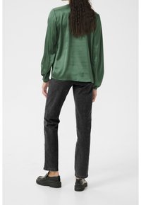 Blouse en satin vert à manches longues, associée à un jean noir droit et des chaussures à plateforme noires. Design simple, sans motifs visibles.