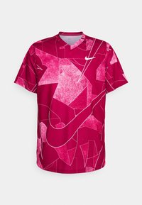 Czerwony sportowy T-shirt z geometrycznym abstrakcyjnym wzorem w kolorze różowym i białym. Krótkie rękawy, dekolt w serek oraz białe logo Nike na piersi.