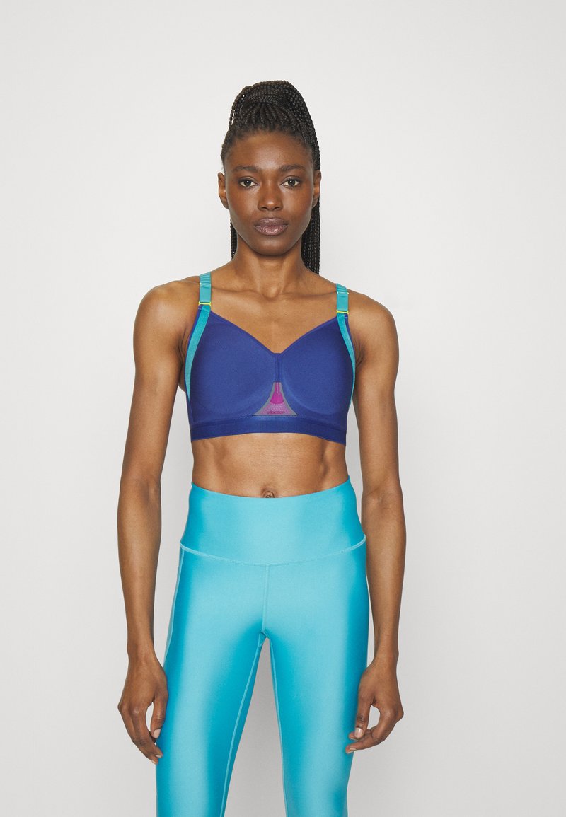 Sujeción deportiva azul marino con tirantes color verde azulado, que cuenta con un panel de malla y un diseño estructurado. Combinado con leggings brillantes color turquesa de cintura alta.