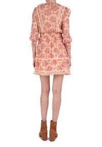 Blumenkleid in hellem Pfirsich mit Dreiviertel-Puffärmeln, gerafftem Taillenbereich und Spitzenakzenten; getragen mit braunen Wildleder-Ankle Boots.