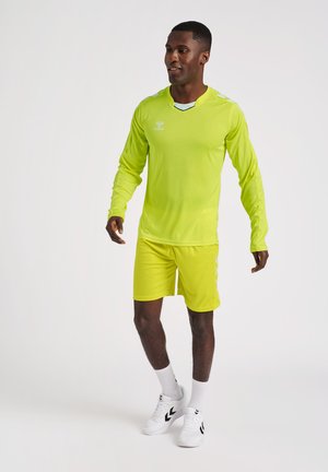 Neon grøn atletisk skjorte med lange ærmer, matchende shorts og hvide sneakers. Har et åndbart stof og minimale branding-akkenter.