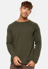 Chemise à manches longues côtelée vert olive avec un col rond et un tissu texturé, mettant en avant des coutures contrastées et une coupe régulière.