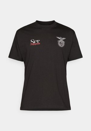 Camiseta de algodón negra con mangas cortas, que presenta texto en blanco y rojo y un logotipo gráfico en el área del pecho izquierdo. Cuello redondo.