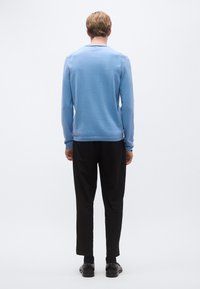 Világoskék hosszú ujjú pulóver bordázott szegéllyel, fekete nadrággal párosítva. Egyszerű kialakítás, puha textúra és kényelmes szabás.