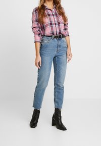 Rosa och marinrutigt skjorta med långa ärmar, knappat krage, kombinerat med hög midja blå jeans och svarta klackboots.