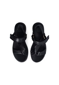 Black sandals with a textured leather material, featuring cross straps and a flat sole. Accented with gold-tone hardware at the straps.