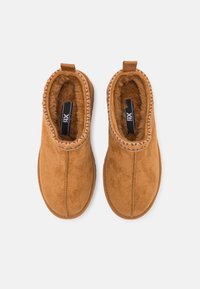 Botas de tobillo de ante marrón con suave forro de piel y ribete de tejido estampado alrededor de la abertura. Cuentan con una lengüeta para facilitar su uso.