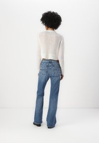 Suéter blanco recortado con punto texturizado y dobladillo acanalado, combinado con jeans azules de cintura alta y acampanados que cuentan con bolsillos traseros.