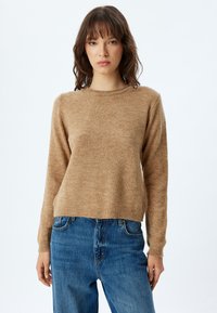 Pull beige à manches longues, col rond, texture douce et coupe légèrement cropped, associé à un jeans en denim bleu.