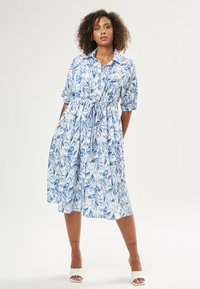 Abito floreale blu e bianco con maniche corte, chiusura a bottoni davanti e vita con cordoncino. Tessuto leggero con una vestibilità comoda.